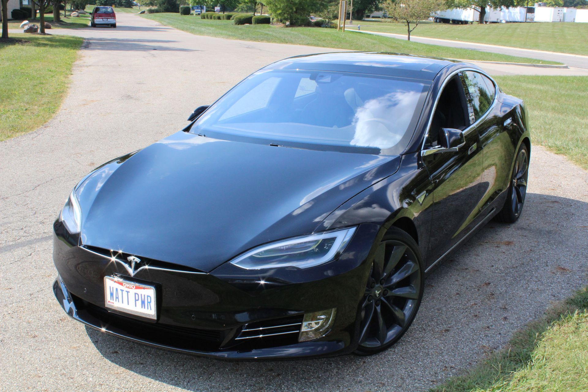 Black Tesla sedan parked on a driveway near grass and trees