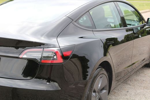 Black Tesla sedan parked outdoors, rear-left view