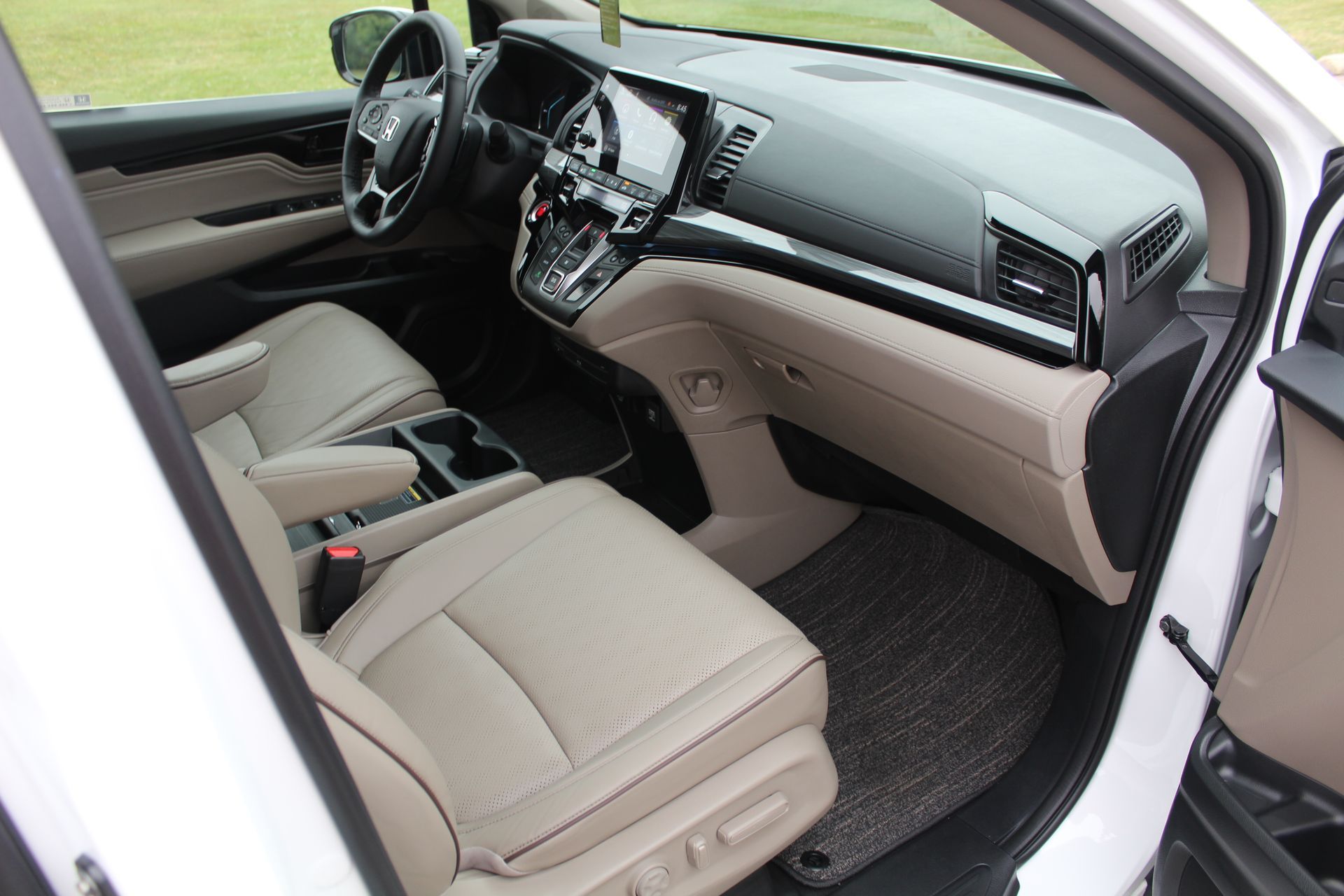 Open car door showing beige leather front seats and dashboard interior in a gray vehicle
