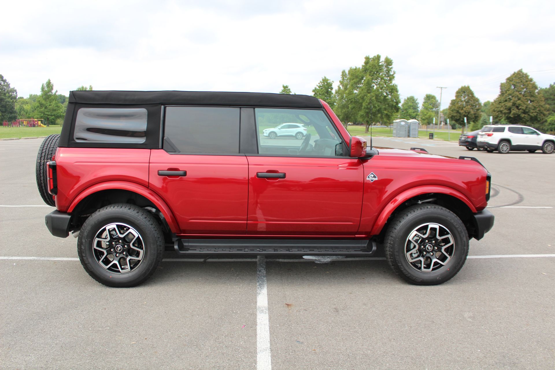Red off-road SUV parked in a lot, side view on a paved surface with trees in the background
