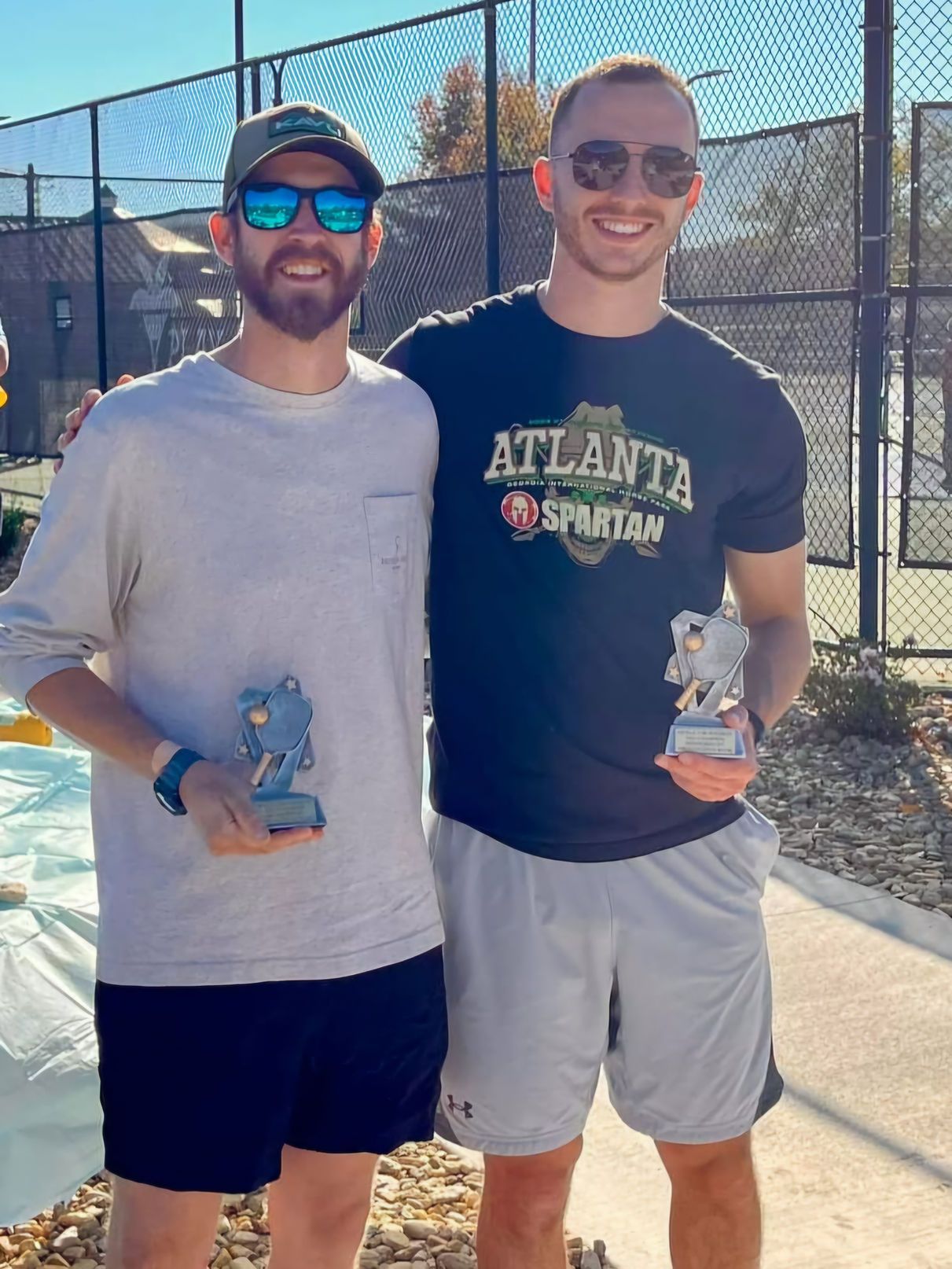 Two men are standing next to each other on a tennis court holding trophies.