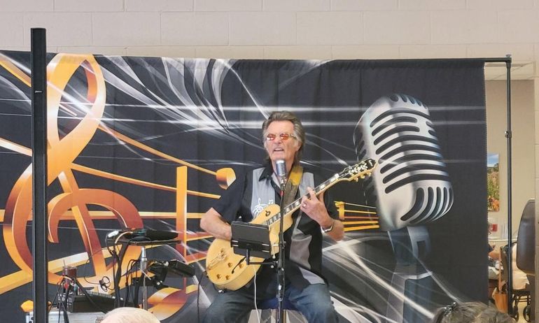 Kenny Laursen  playing guitar on stage in front of a large microphone backdrop