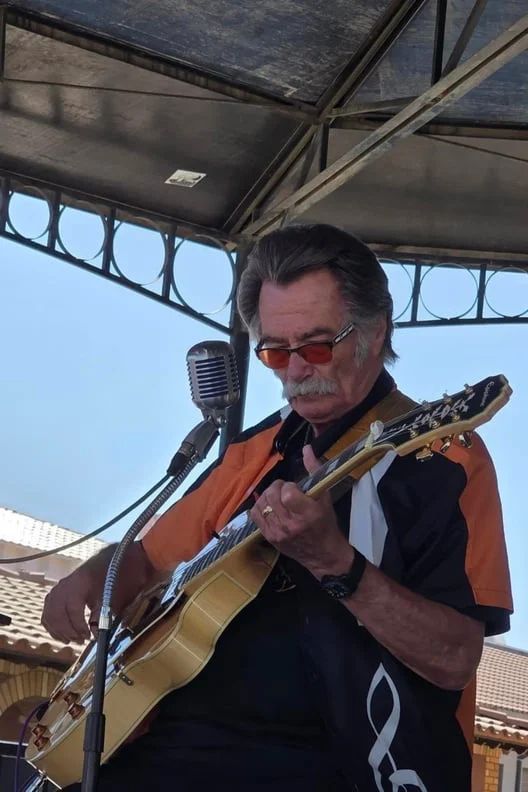 Kenny Laursen playing guitar and singing under a metal-roofed outdoor stage