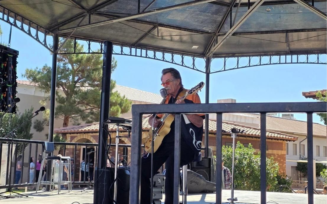 Kenny Laursen playing guitar on an outdoor stage under a gazebo