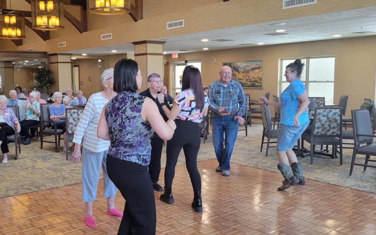 People dancing in a banquet hall with wooden floors and chairs around the room.