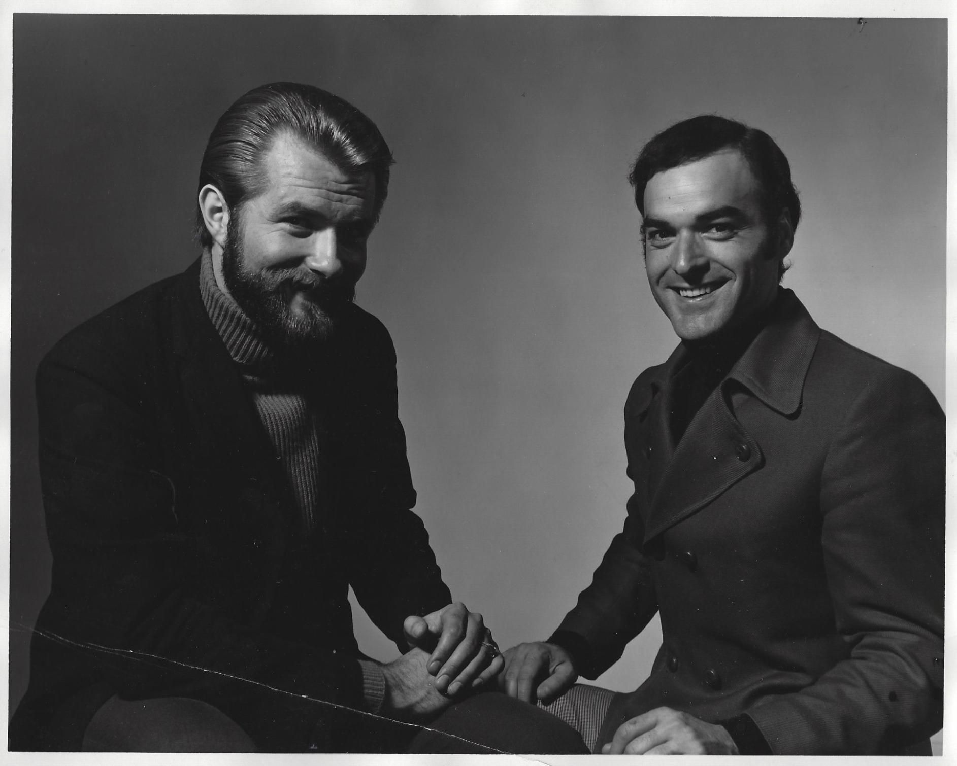 Two men seated and smiling in a black-and-white studio portrait.