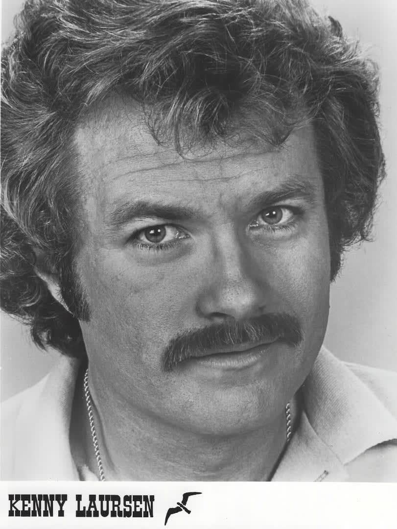 Black-and-white portrait of a man with wavy hair and a mustache, looking at the camera.
