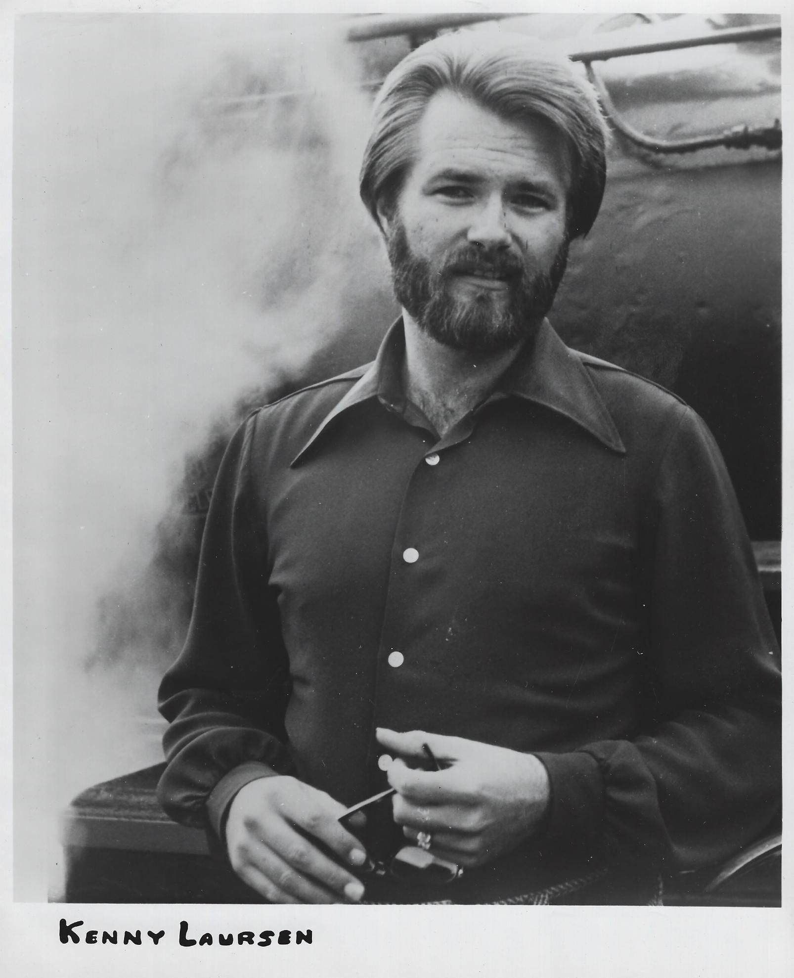 Bearded man in a dark shirt standing beside a steaming train