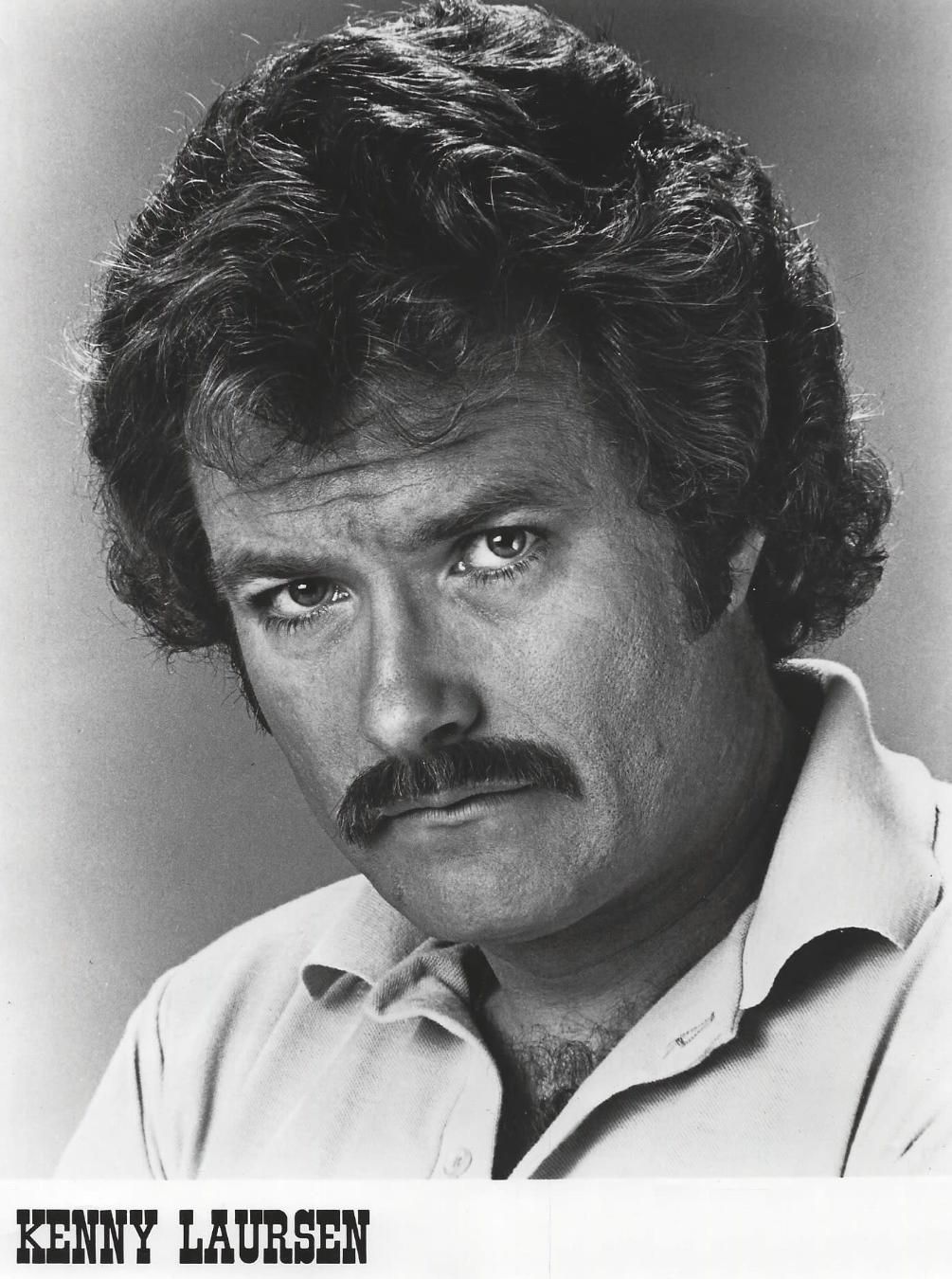 Black-and-white portrait of a man with a mustache, gazing at the camera.