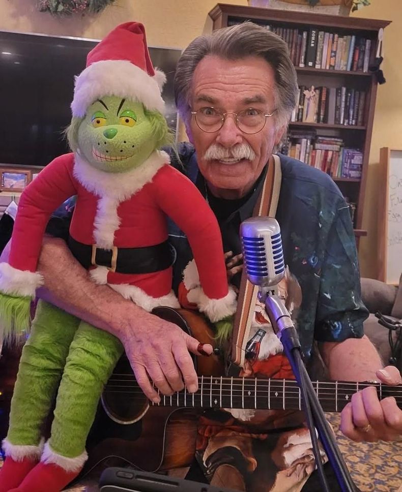 Kenny Laursen playing guitar with a Grinch plush in Santa outfit