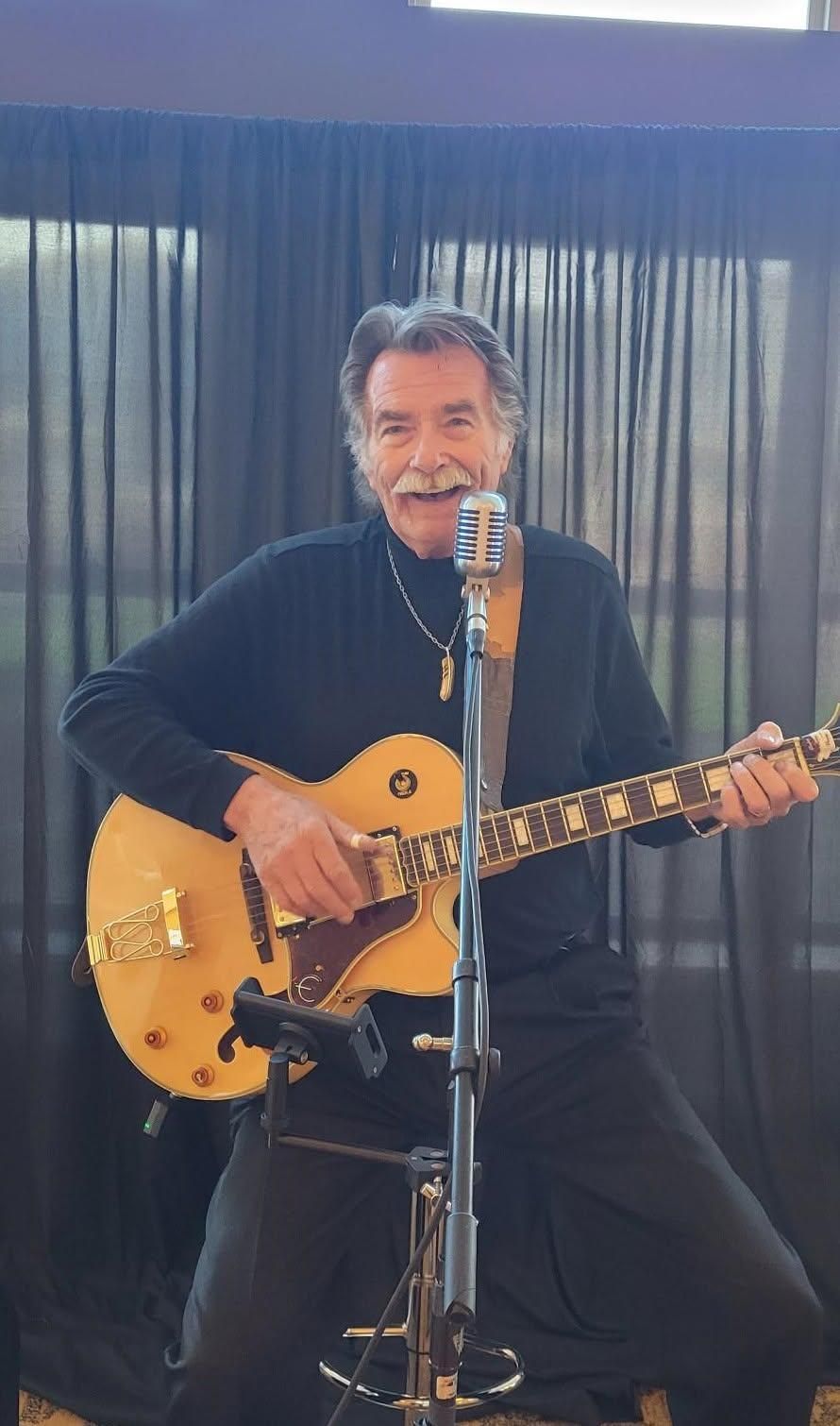 Kenny Laursen playing acoustic guitar and singing into a microphone