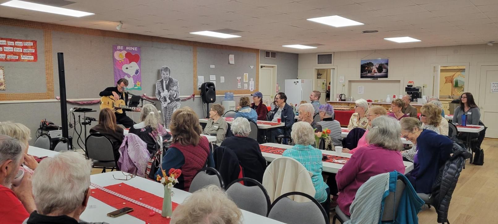 Community room filled with people seated at tables for a social gathering or event