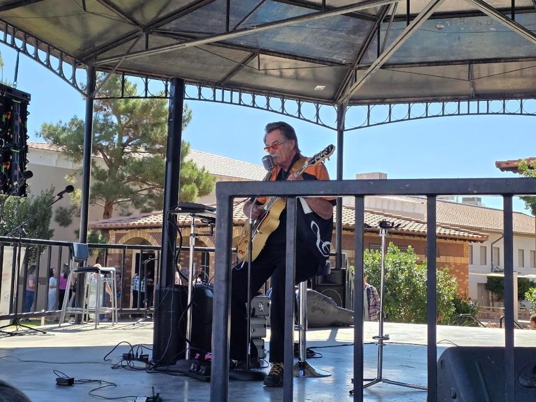 Kenny Laursen playing guitar on an outdoor stage under a canopy