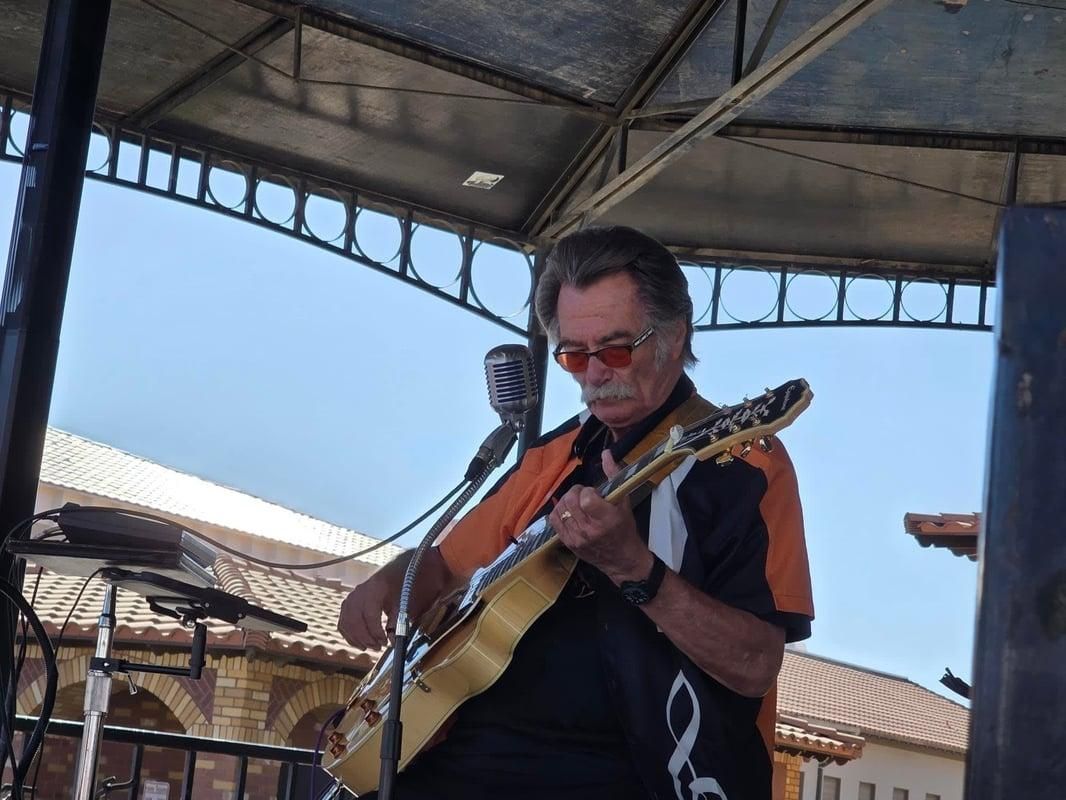 Kenny Laursen playing guitar and singing into a microphone on an outdoor stage
