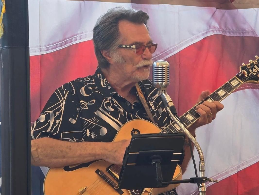 Kenny Laursen singing into a vintage microphone while playing guitar
