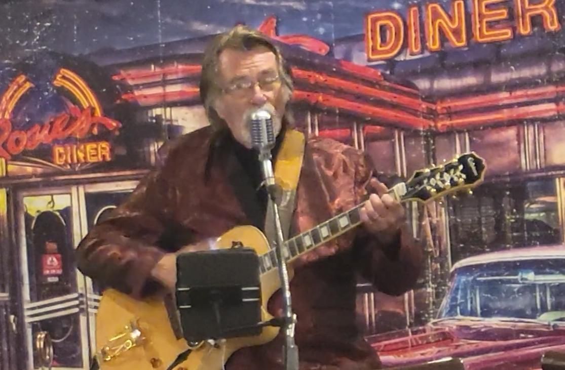 Kenny Laursen singing into a microphone while playing guitar