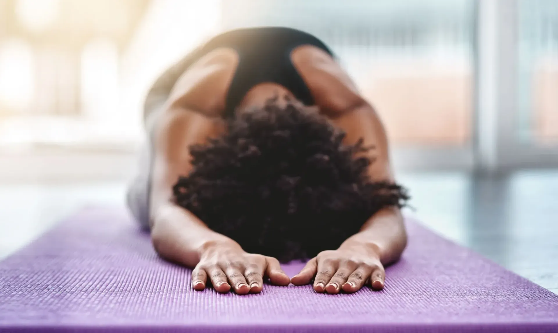 Person doing child’s pose on a purple yoga mat in a bright room at The Summit at the Reserve in Round Rock Texas.