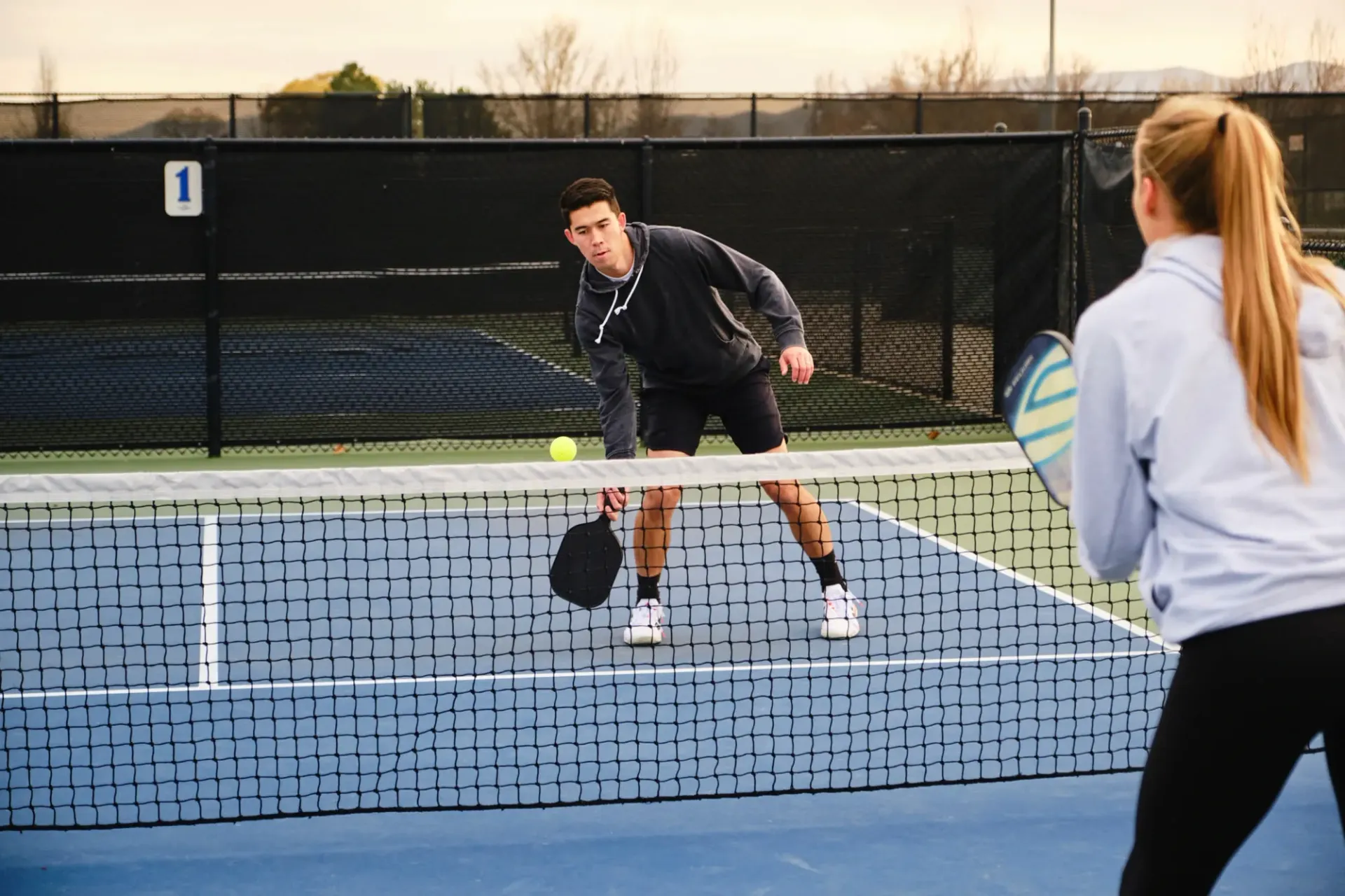 Two players rally on an outdoor pickleball court, one near the net at The Summit at the Reserve in Round Rock Texas.