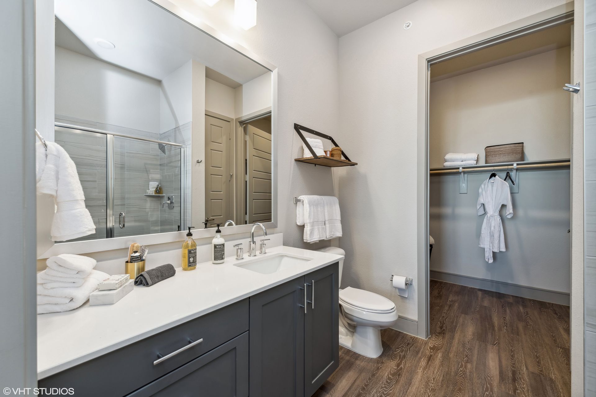 Modern bathroom with double vanity, large mirror, toilet, and open closet with hanging clothes.