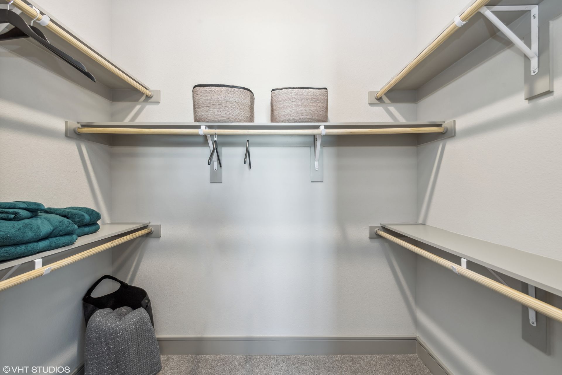 Empty walk-in closet with white shelves, hanging rods, and a few folded towels and storage baskets
