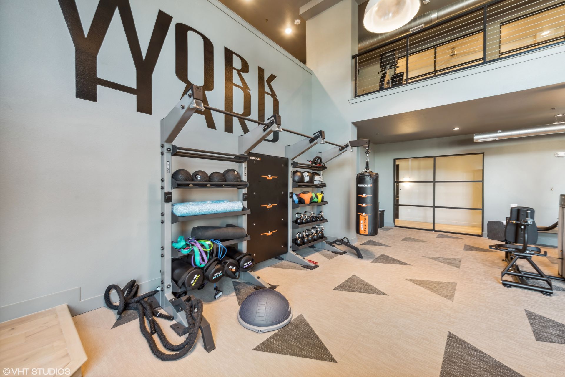 Modern gym room with exercise equipment, large “WORK” wall art, and a loft balcony overhead