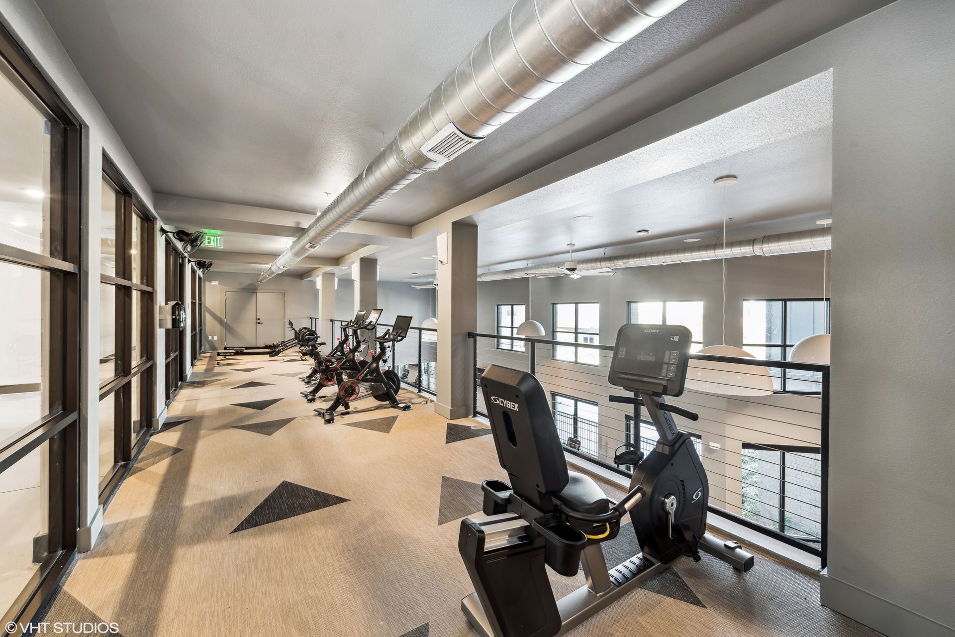 Modern gym corridor with exercise bikes, large windows, and bright overhead lighting