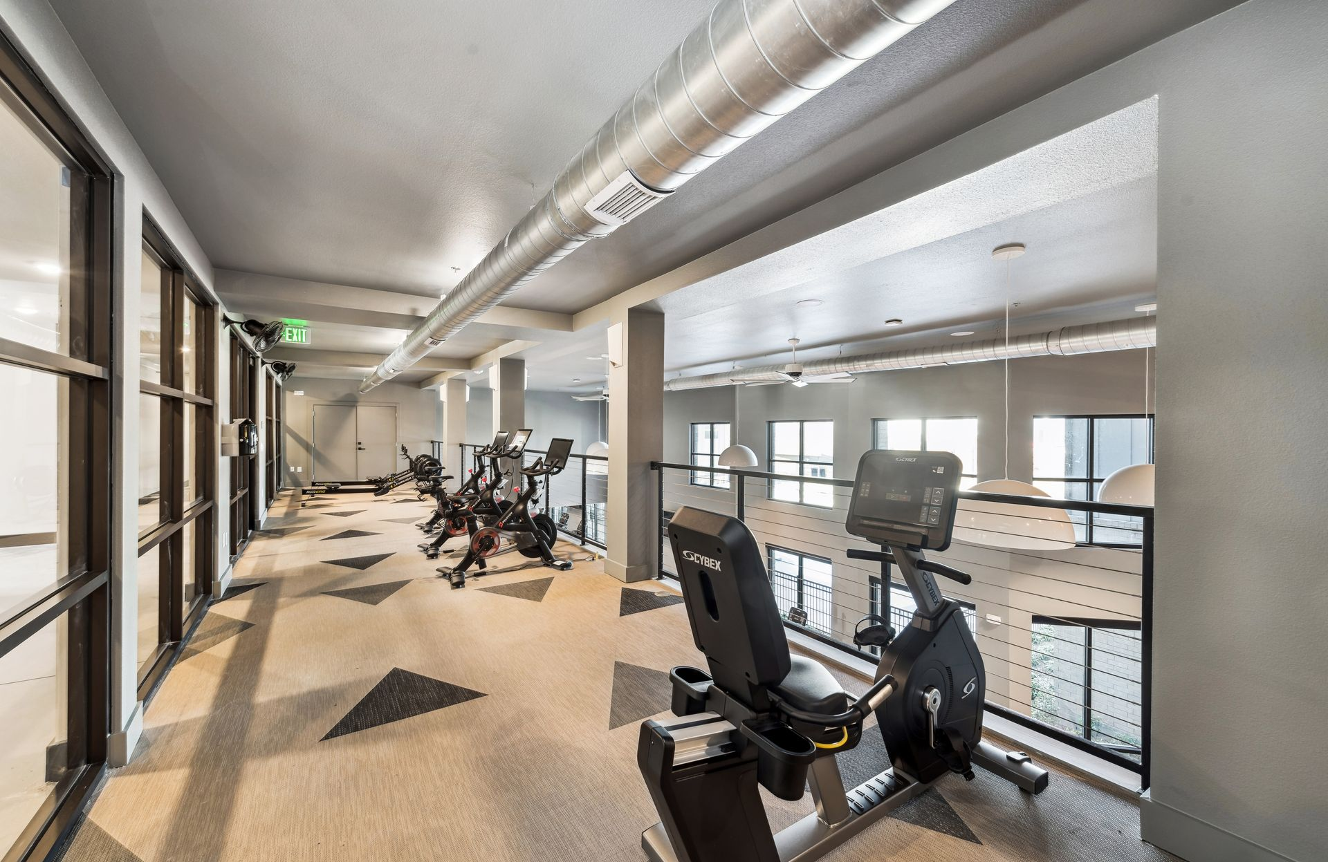 Modern gym with cardio machines beside a glass wall in a bright hallway
