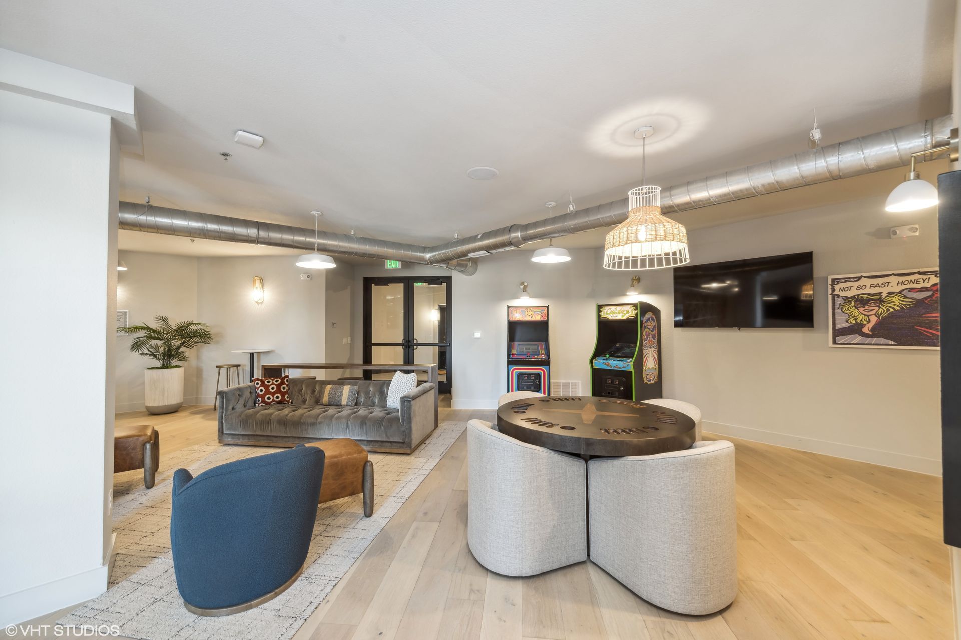 Modern open-plan living room with light wood floors, gray seating, TV, and dining area