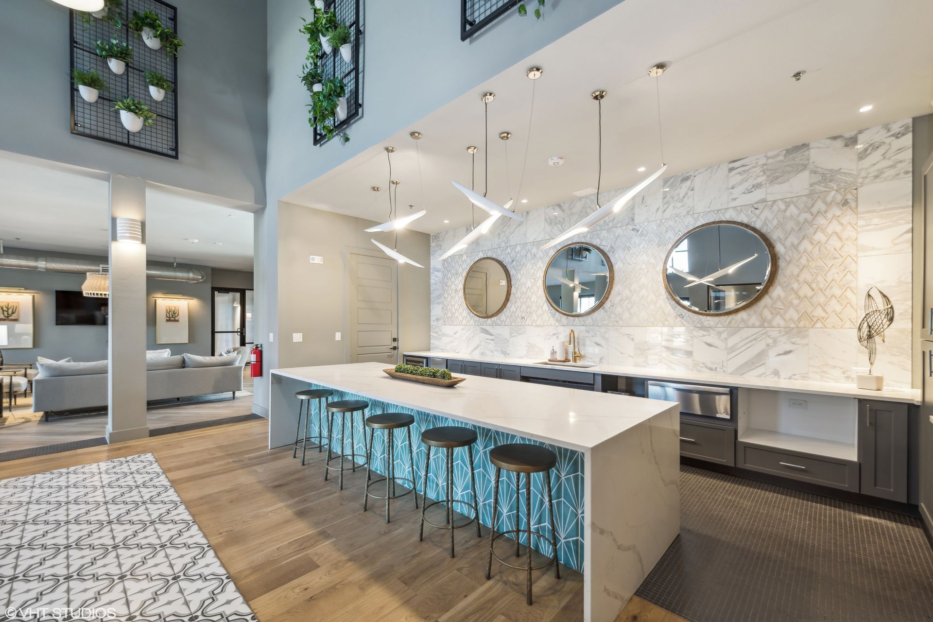 Modern kitchen with marble island, teal stools, and round mirrors on a white brick wall
