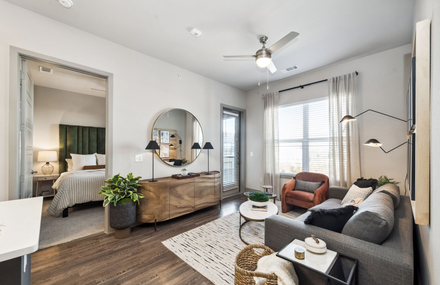 Bright living room with gray sofa, patterned rug, wood sideboard, and armchair by sunlit windows