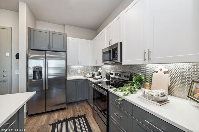 Modern kitchen with stainless steel appliances, white cabinets, gray lower cabinets, and mosaic backsplash