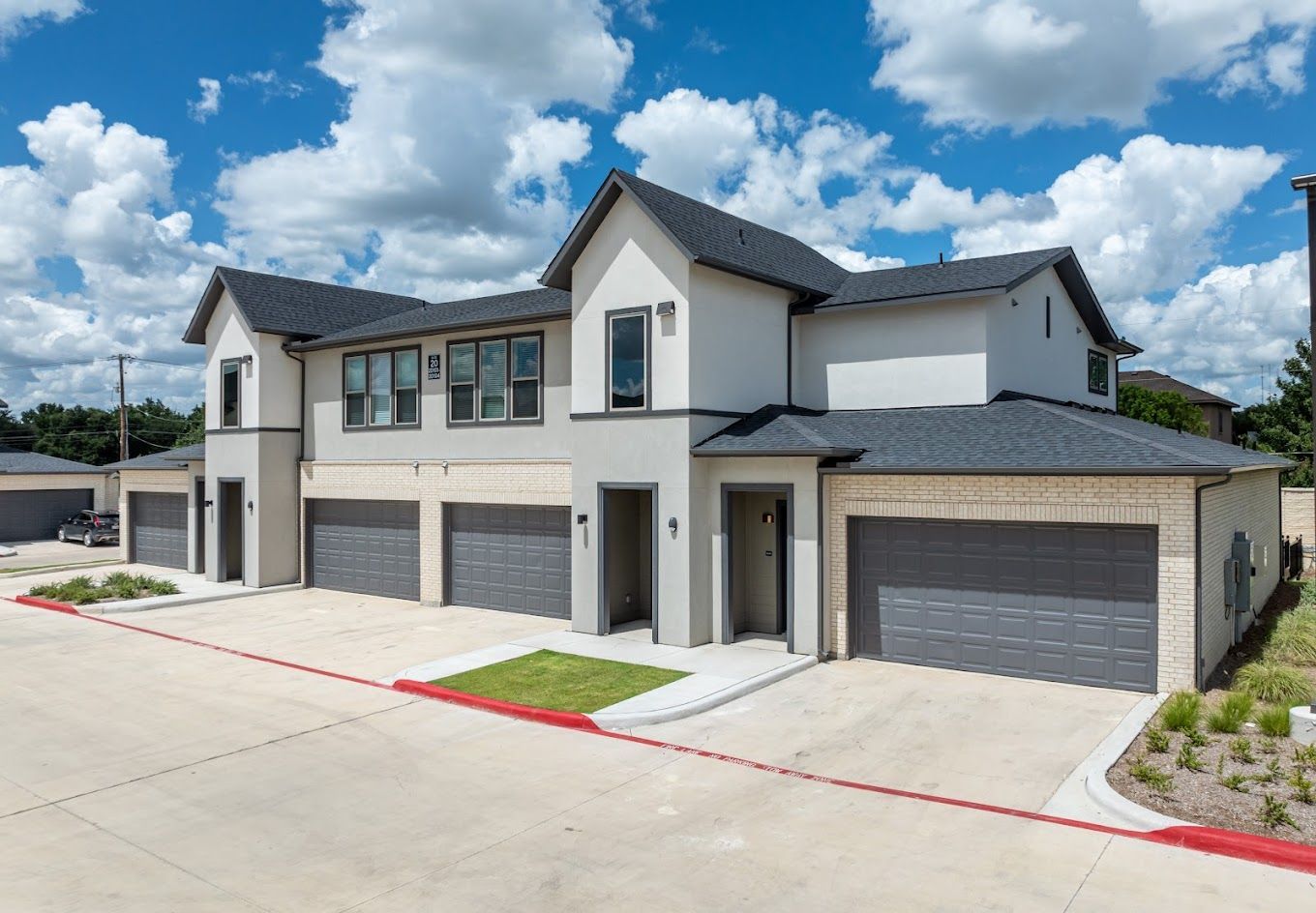 Modern two-story townhouse with attached garages under a partly cloudy blue sky