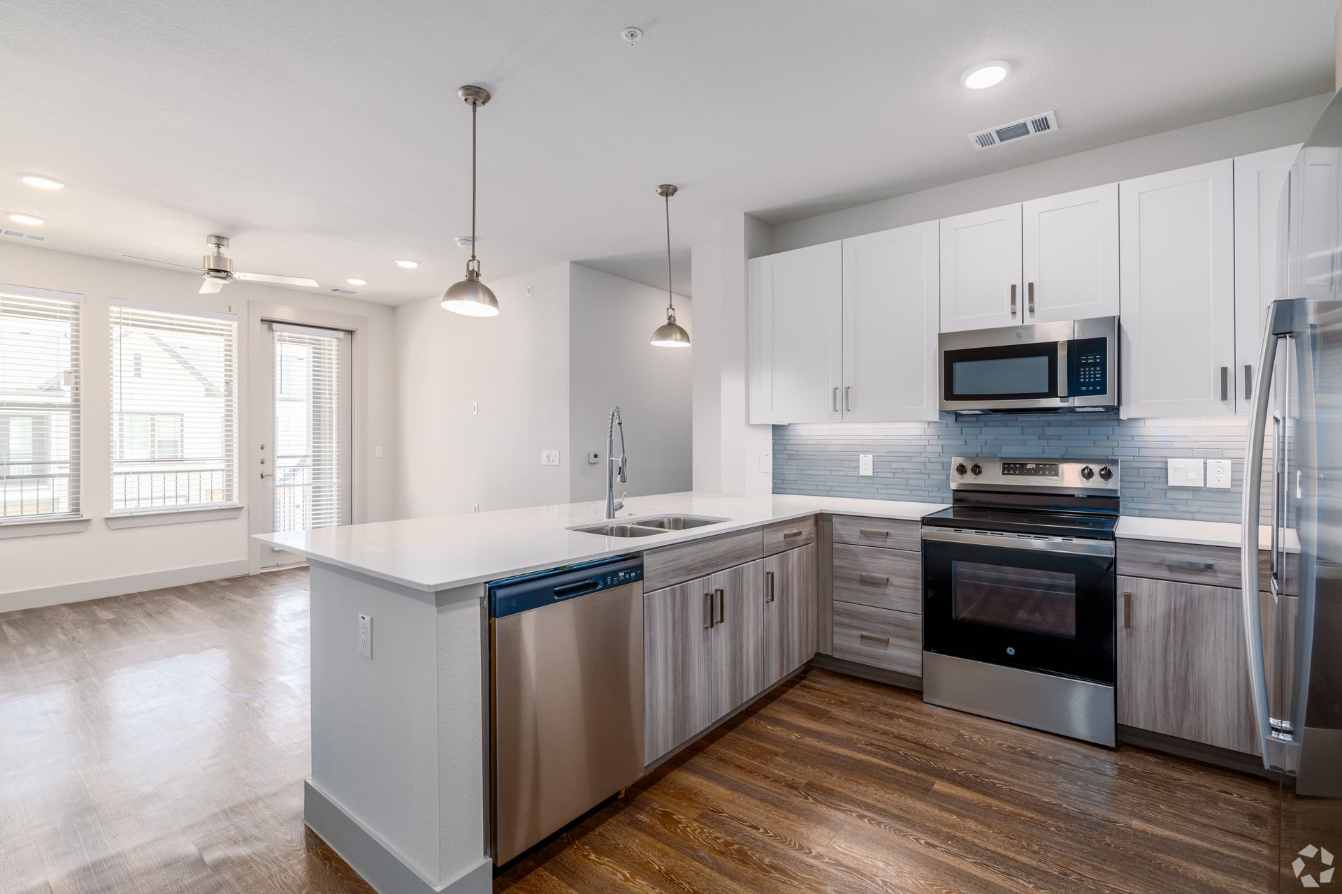 Bright modern kitchen with white cabinets, stainless appliances, and wood floors in an open living space