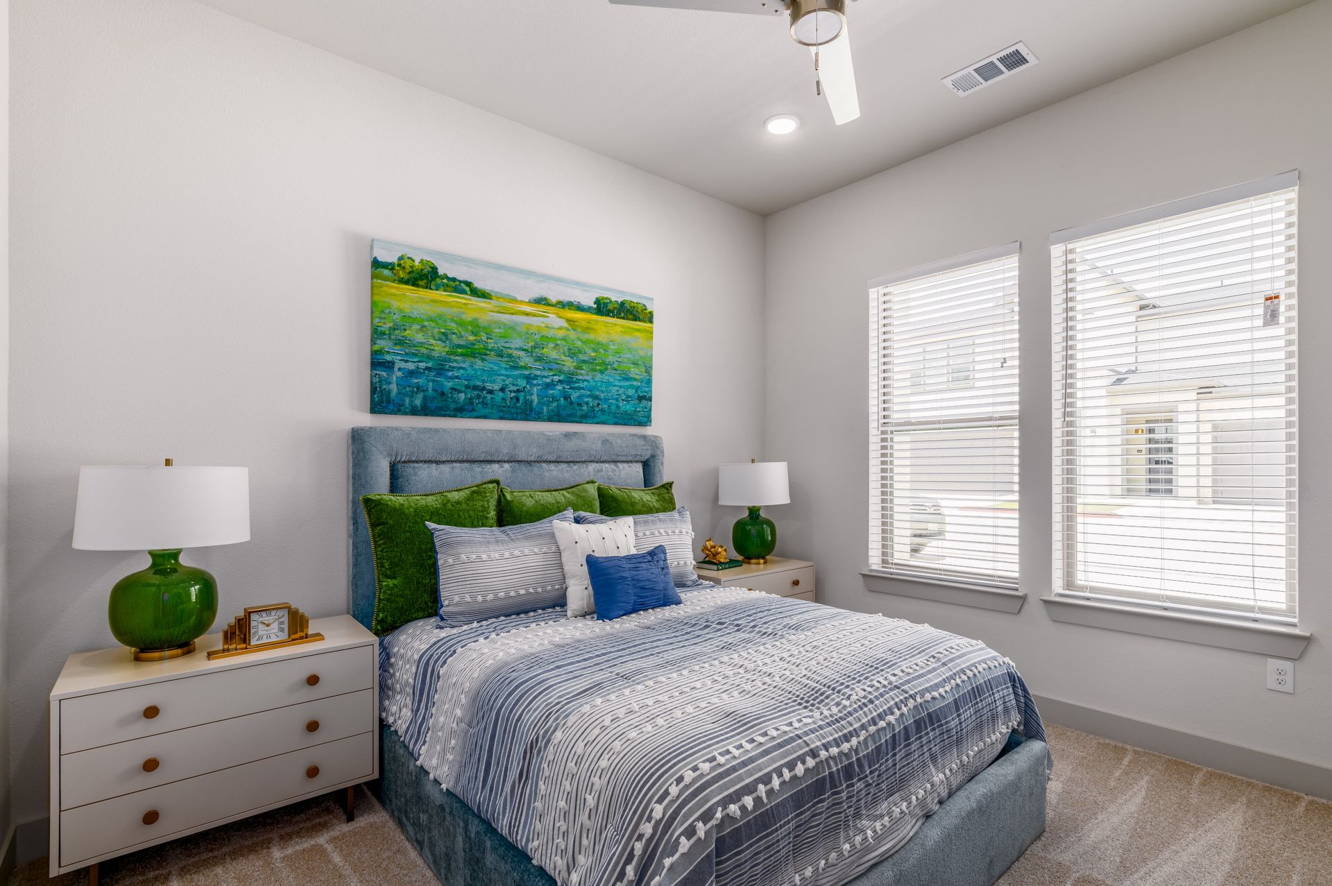 Bright bedroom with a bed, green accents, white dresser, and windows with blinds