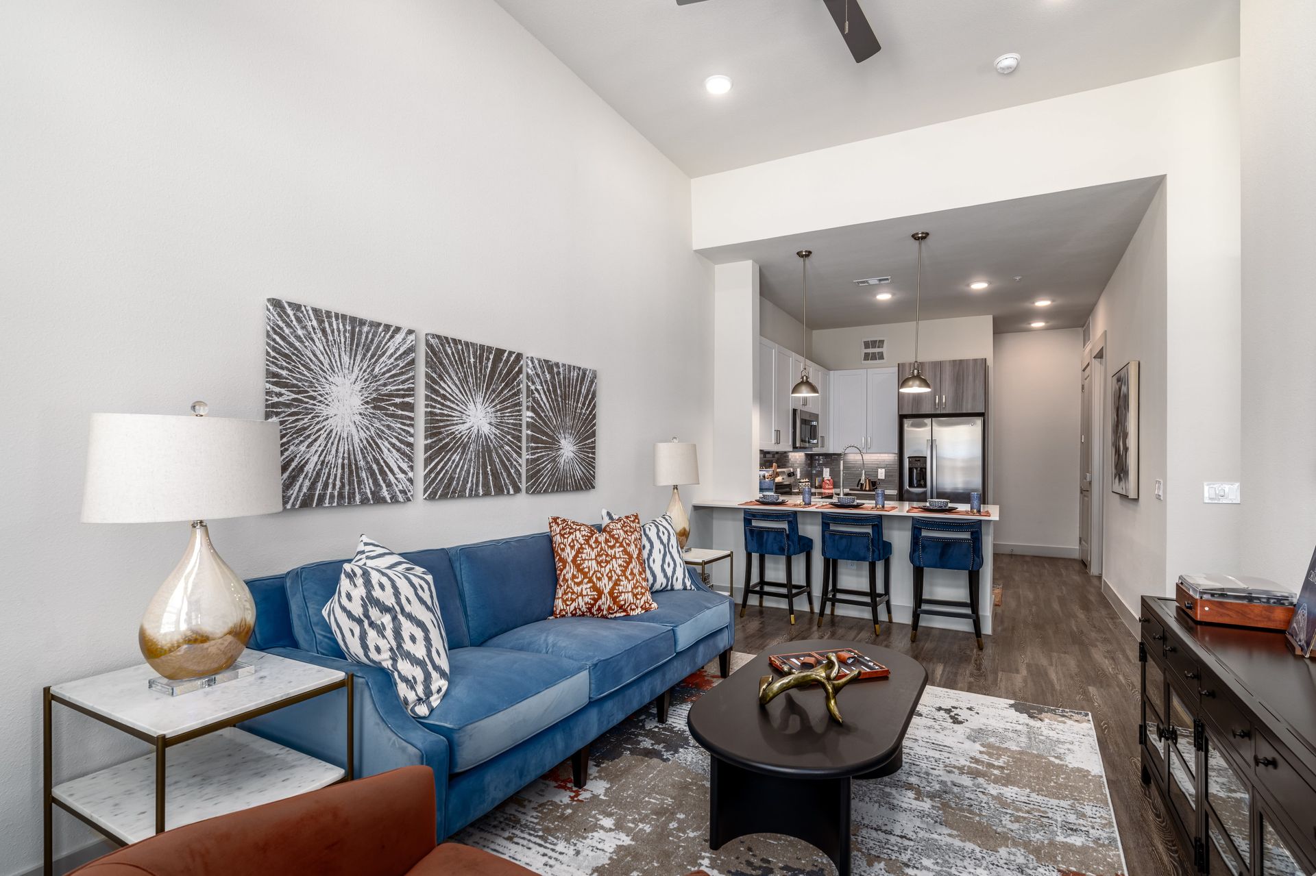 Bright modern living room with blue sofa, patterned rug, and open kitchen beyond