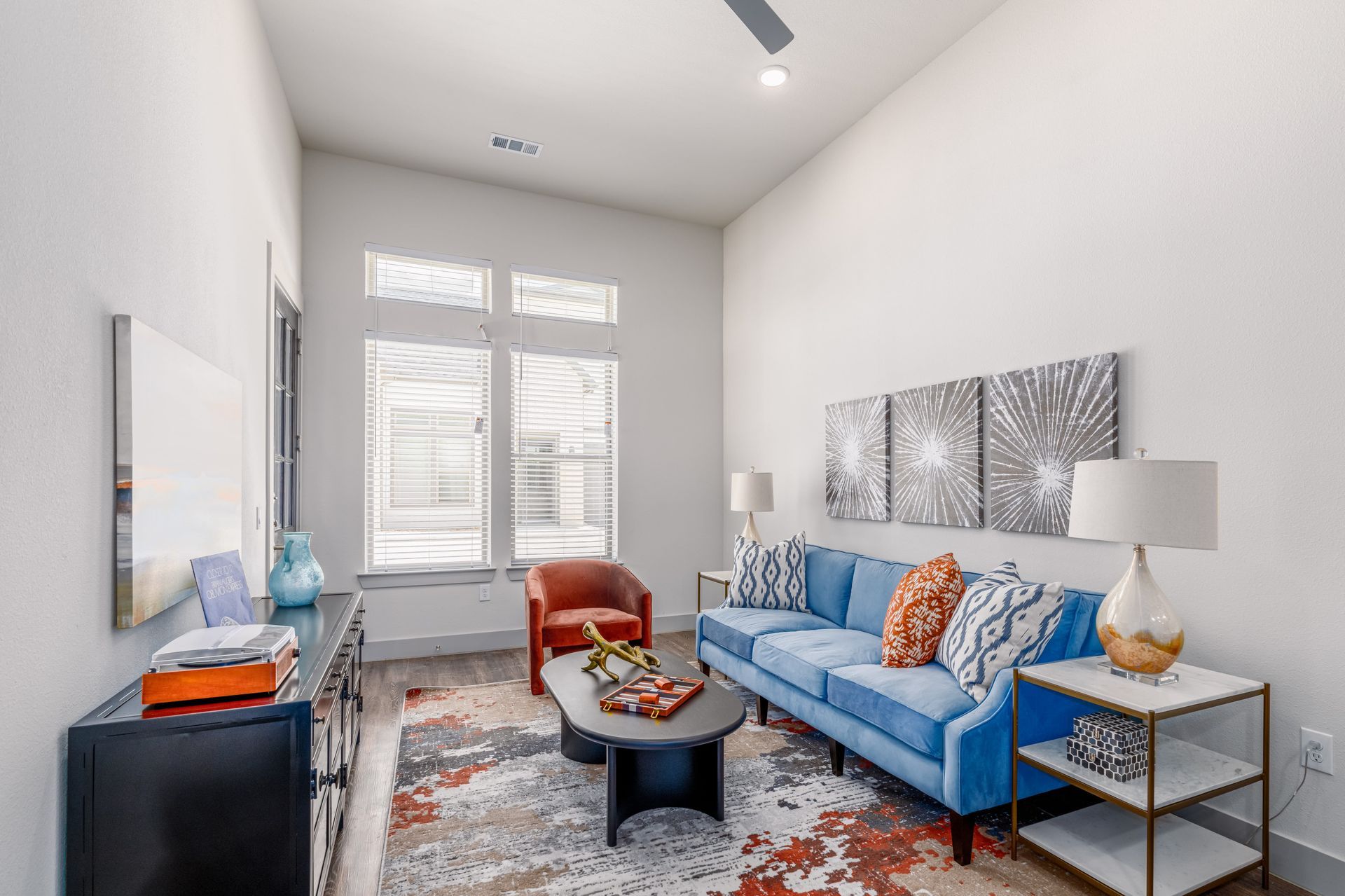 Bright living room with blue sofa, armchair, patterned rug, and large windows.
