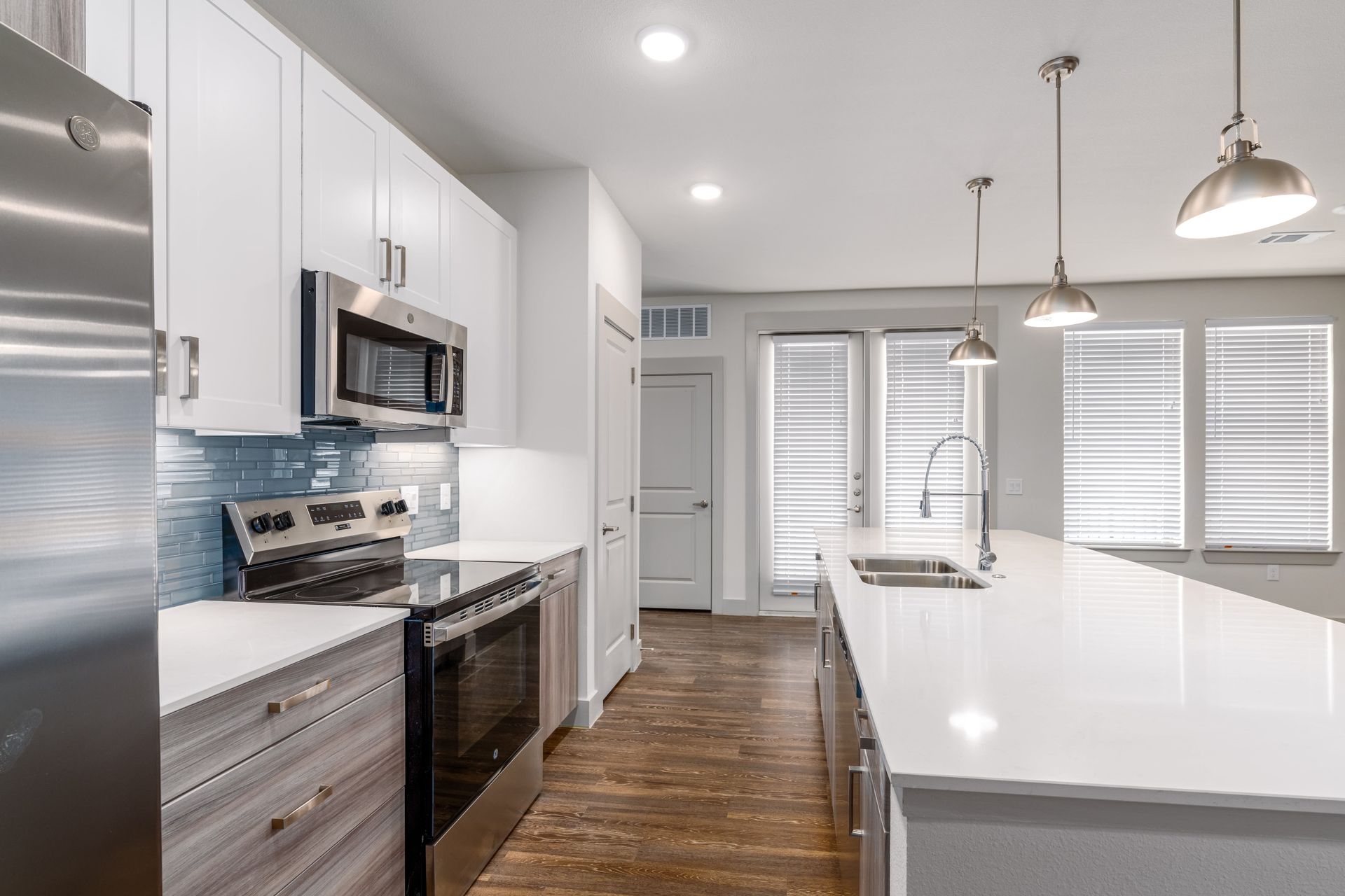 Bright white modern kitchen with stainless appliances, wood floor, and large island sink