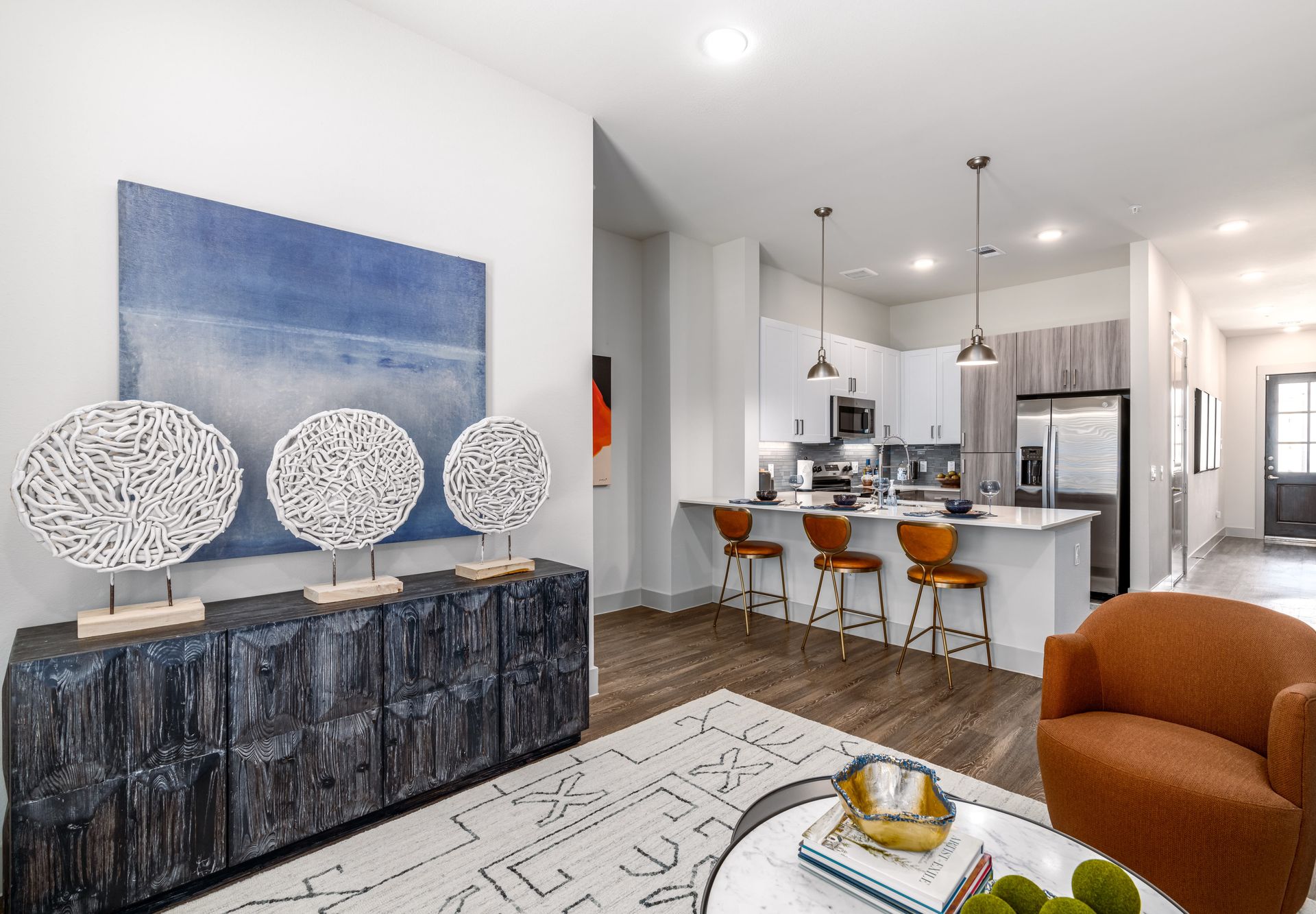 Bright open living room with blue wall art, orange chair, and a modern kitchen with island stools