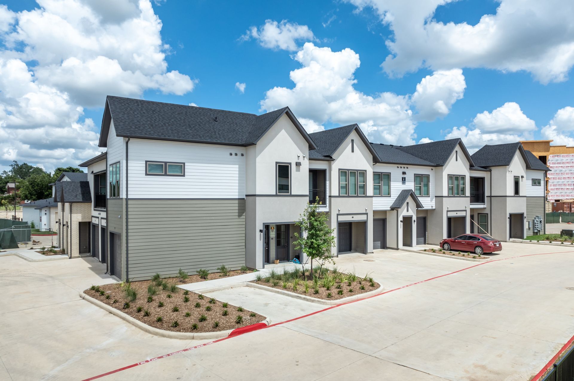 Modern row of white townhouses with gray roofs along a wide street under a blue sky