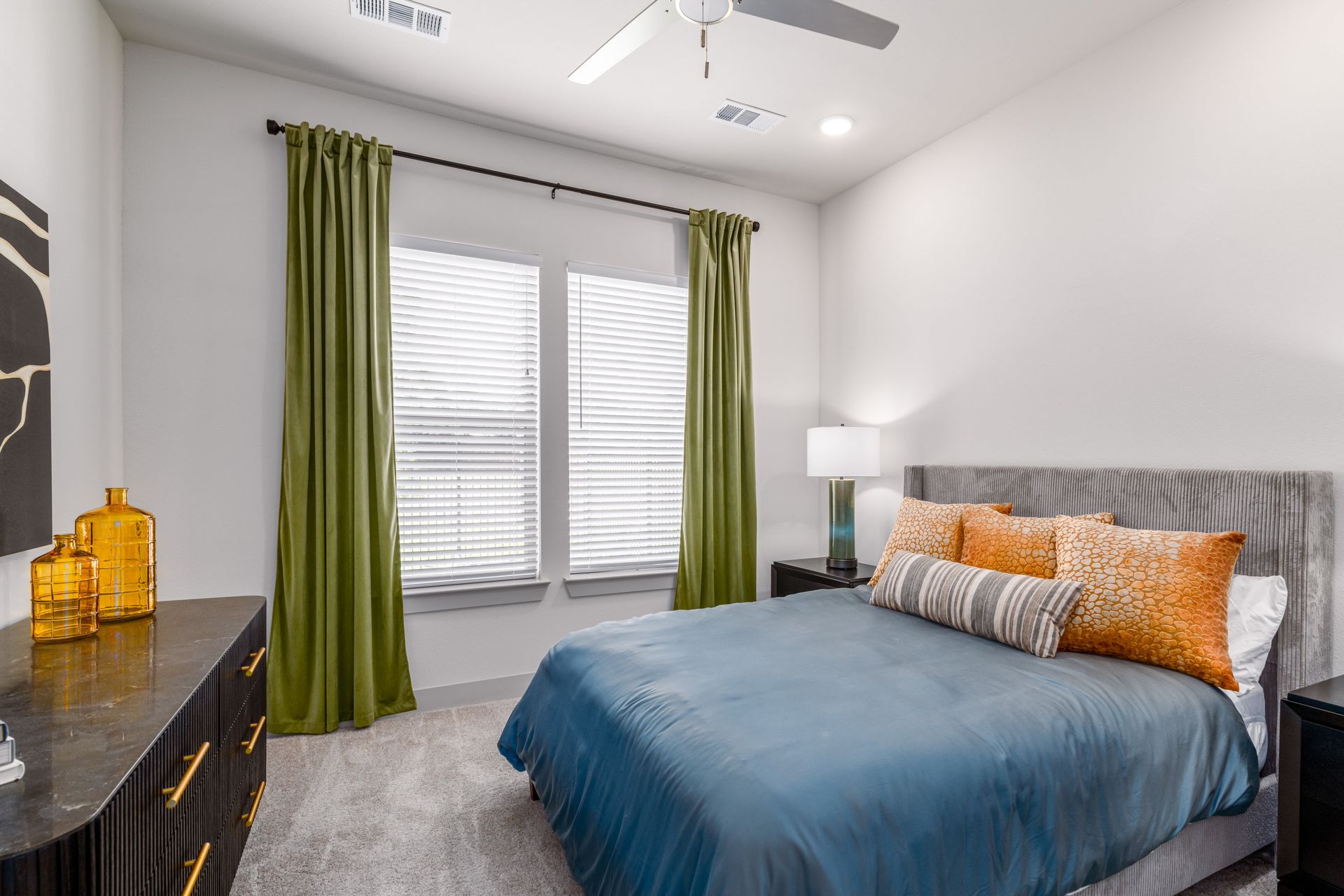 Modern bedroom with blue comforter, green curtains, gray carpet, and a window with blinds