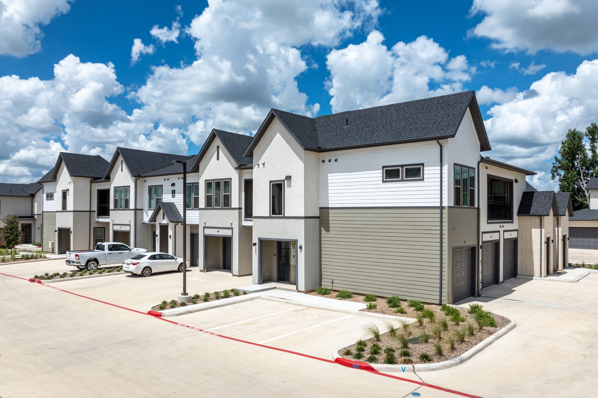 Modern townhouses with white facades and dark roofs along a paved street under a bright blue sky