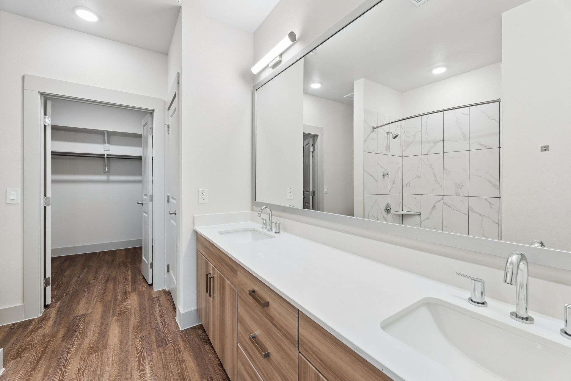 Modern bathroom with double vanity, large mirror, and walk-in closet visible through an open door