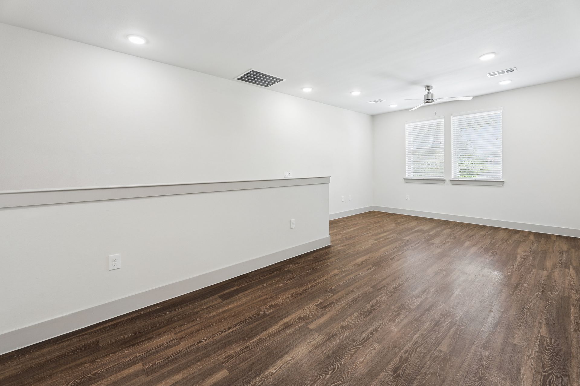 Empty white room with wood floors, recessed lights, and two windows.