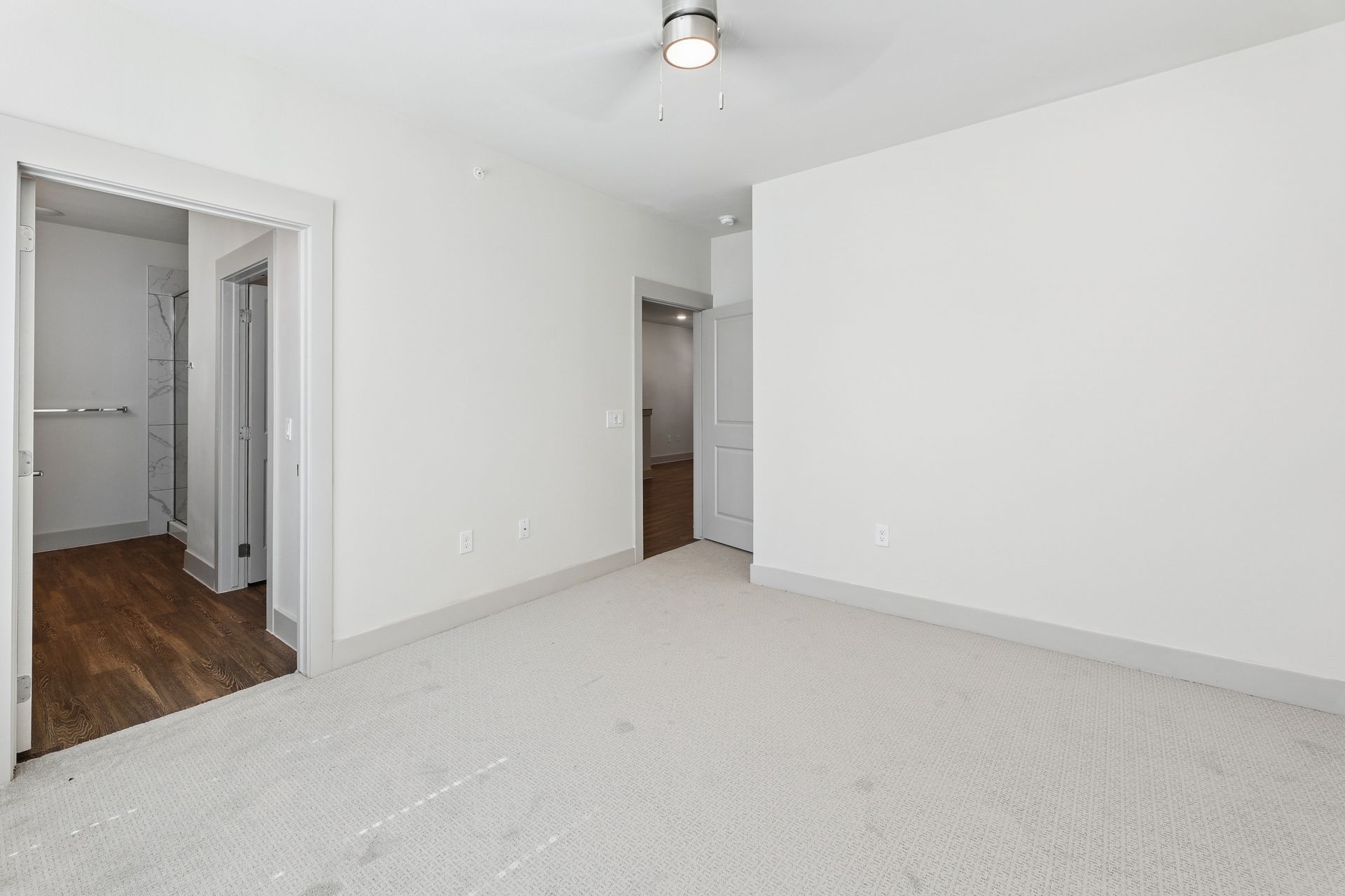 Empty white bedroom with carpet, hardwood hallway, and two doorways