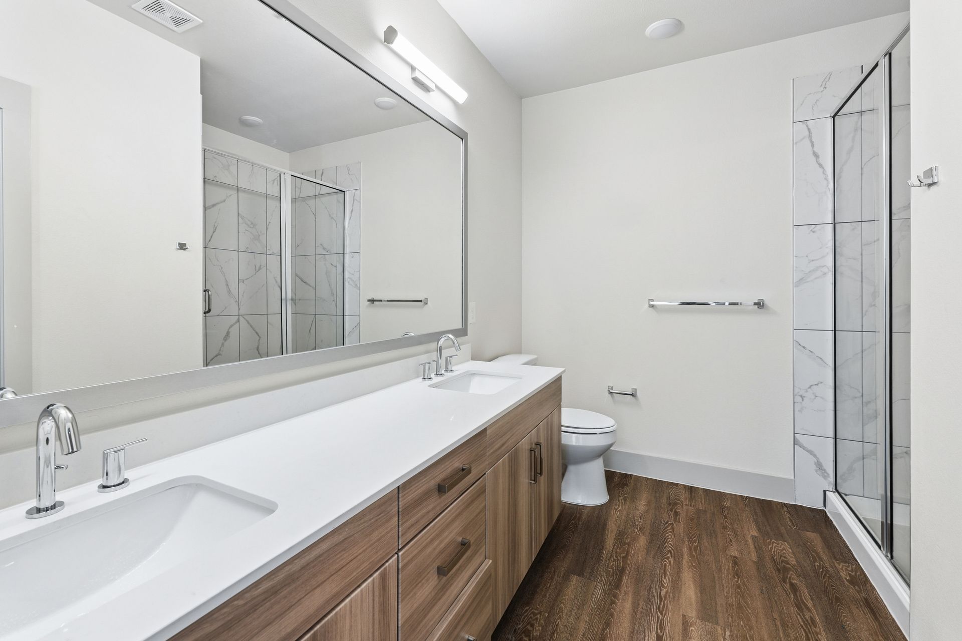 Modern bathroom with double vanity, large mirror, wood cabinets, and a glass-enclosed shower.