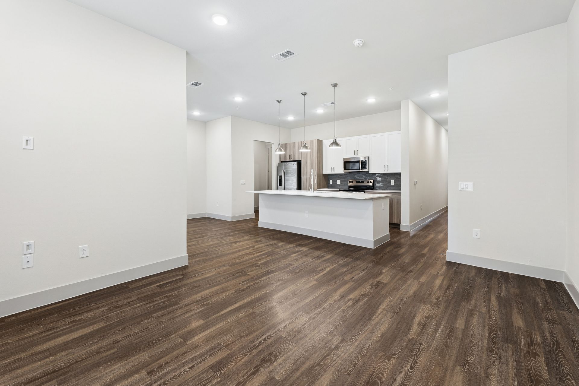 Empty modern kitchen with white cabinets, island, and wood-look flooring in a bright open room