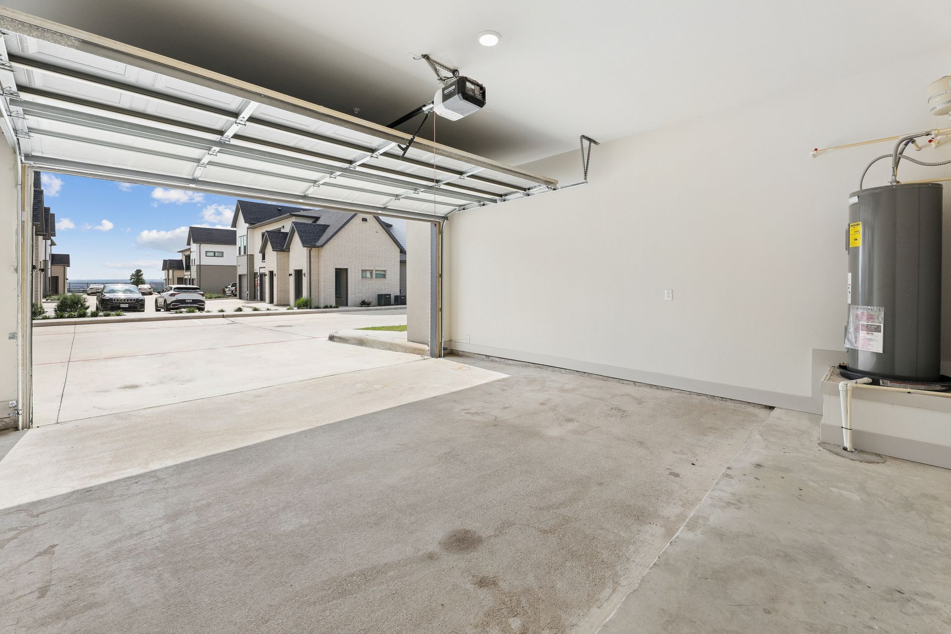 Empty garage interior with open door, concrete floor, and water heater on the right.