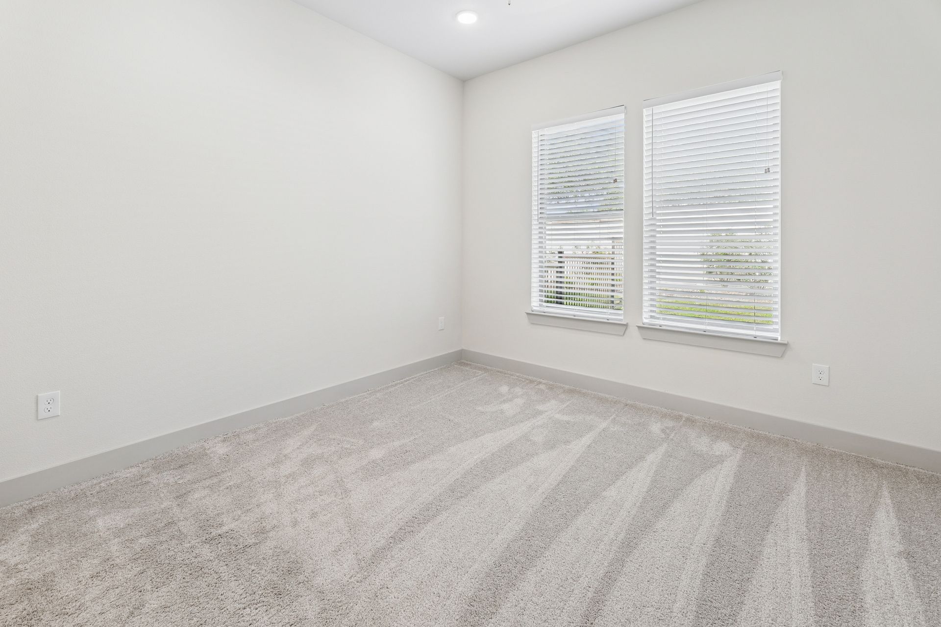 Empty carpeted bedroom with white walls and two windows with blinds