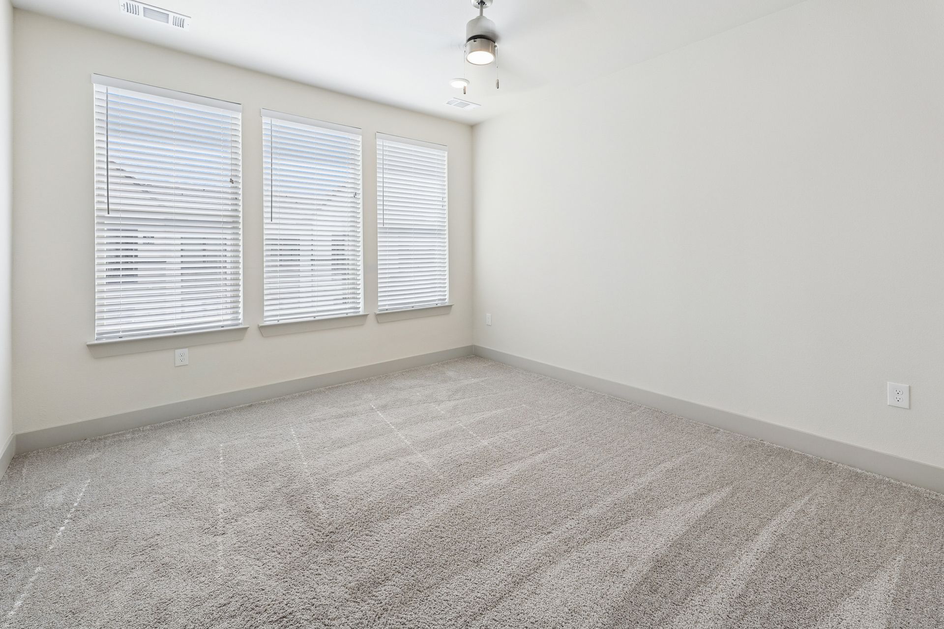 Empty carpeted room with white walls, large window blinds, and ceiling light.