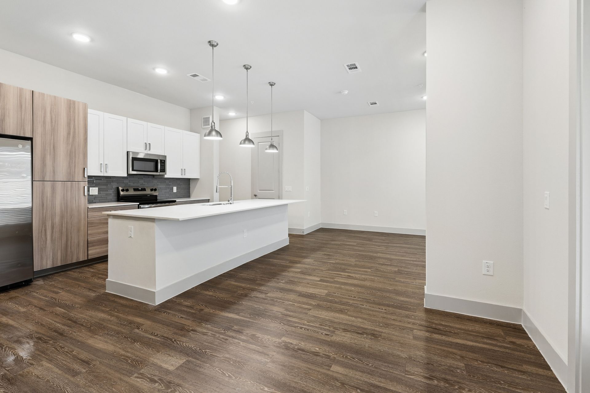 Bright modern kitchen with white island, light wood cabinets, and dark wood floors in an open living space